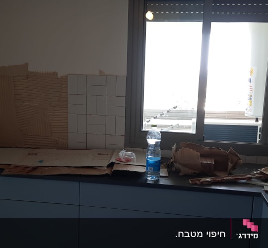 עבודת חיפוי קיר מטבח באריחי קרמיקה לבנים מעל משטח העבודה